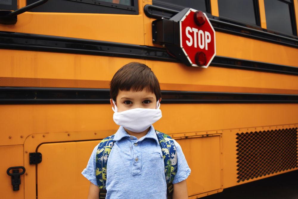 Student in mask next to school bus